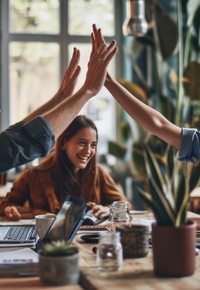 Colleagues are giving each other a high five in an office setting, with big smiles on their faces, indicating a celebration or success.